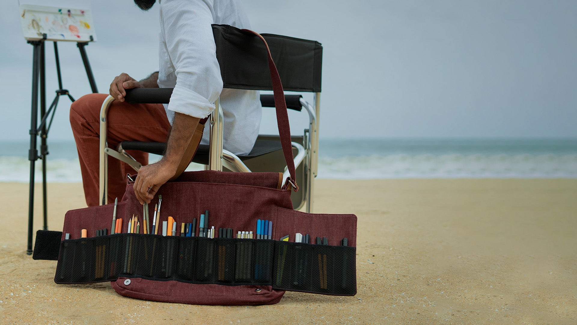 A close up shot of a plein air artist taking out a brush from his open Lilorosh artist bag that neatly holds and displays all his art supplies.