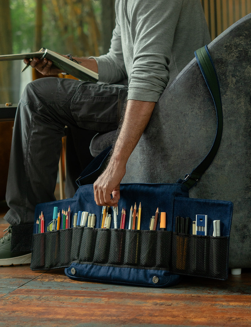 An artist sketching in a cafe, taking a tool from his open Lilorosh artist bag that neatly displays all his art supplies